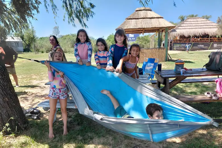 Chicos jugando con una hamaca paraguaya, con el parador de fondo