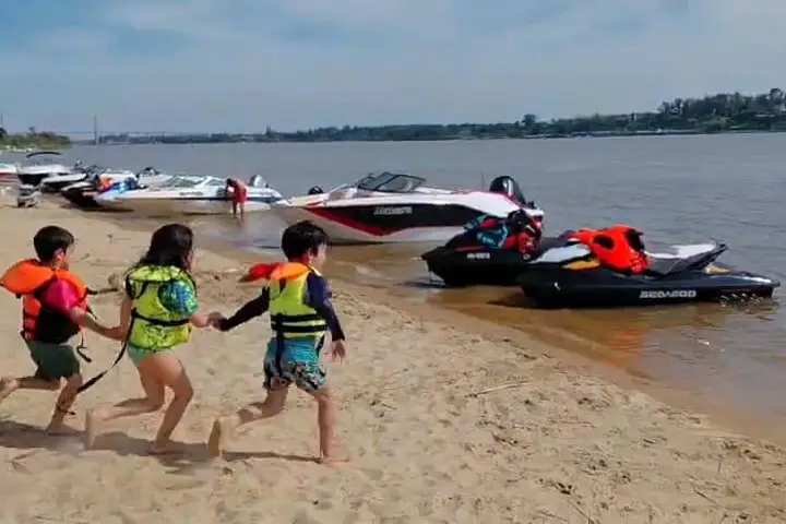 Chicos con chaleco salvavidas corriendo por la playa junto a las motos de agua