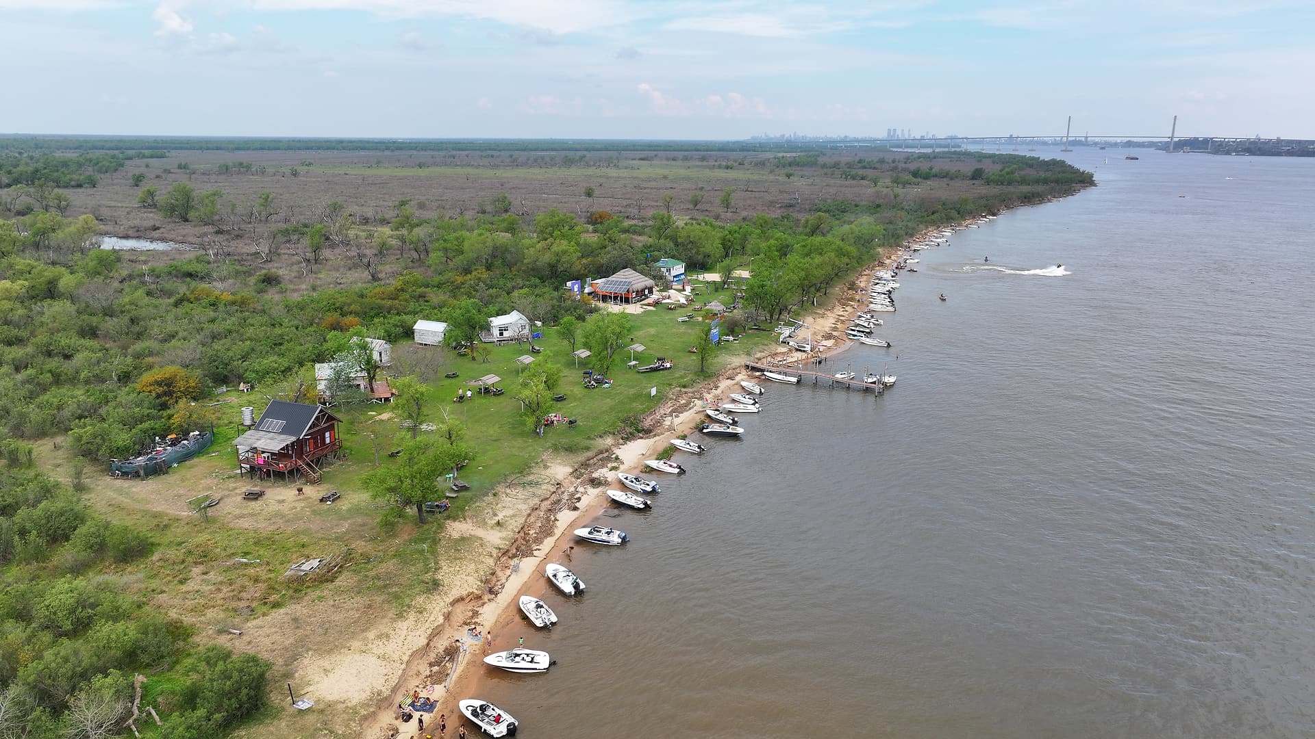 Vista aérea de Puerto Los Mástiles: la costa de la isla con lanchas amarradas sobre el Paraná y el puente al fondo