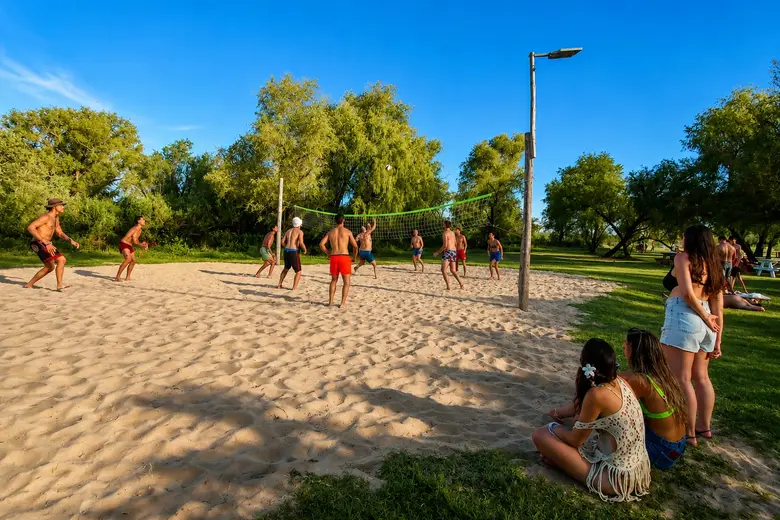 Partido de vóley en la cancha de arena del Puerto, rodeada de árboles
